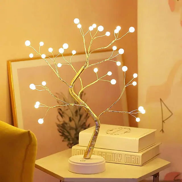 A decorative LED light tree with branches, placed on a circular base, emitting a warm white glow.