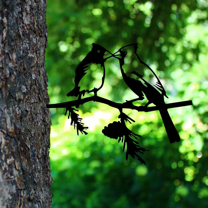 A silhouette of a bird perched on a tree branch, created from metal with a black finish, displayed in a garden setting.