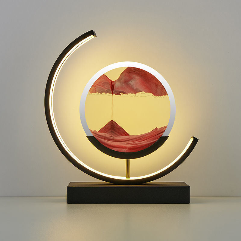 A unique decorative LED desk lamp with a 3D sand art design that creates a serene landscape, placed on a bookshelf in a home environment.