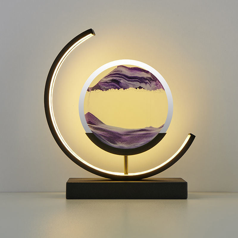 A unique decorative LED desk lamp with a 3D sand art design that creates a serene landscape, placed on a bookshelf in a home environment.