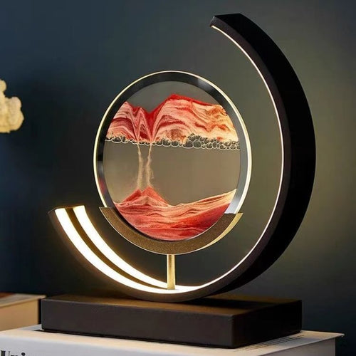 A unique decorative LED desk lamp with a 3D sand art design that creates a serene landscape, placed on a bookshelf in a home environment.